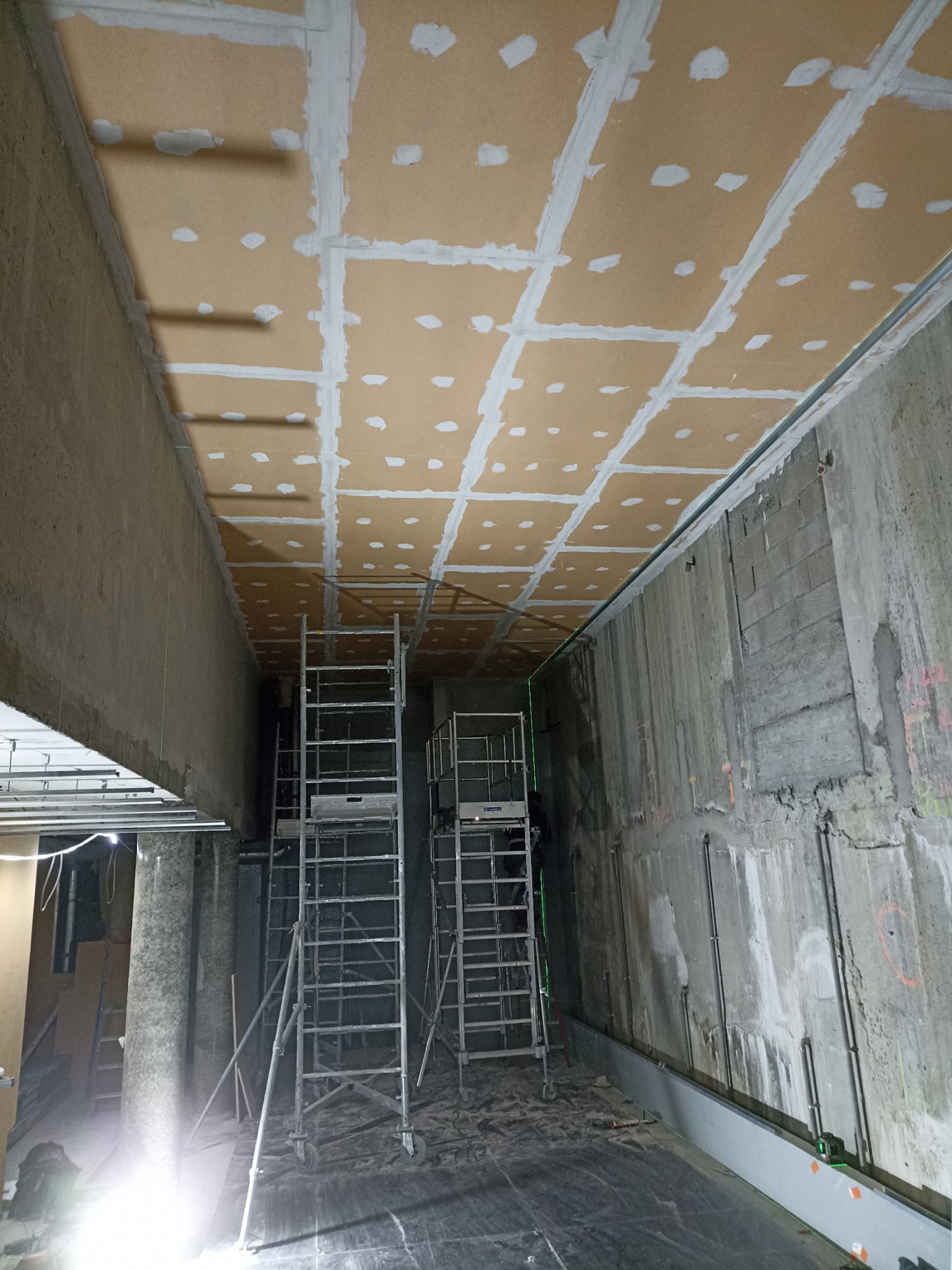 Montaż sufitu z płyt karton gips z widocznymi łączeniami szpachlowanymi, rusztowania w surowym wnętrzu. Etap prac wykończeniowych.