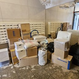 TwojeGraty - Stos kartonów i toreb w holu bloku, przygotowanych do transportu. Widoczne skrzynki pocztowe i drzwi wejściowe. Kartony Castorama.
