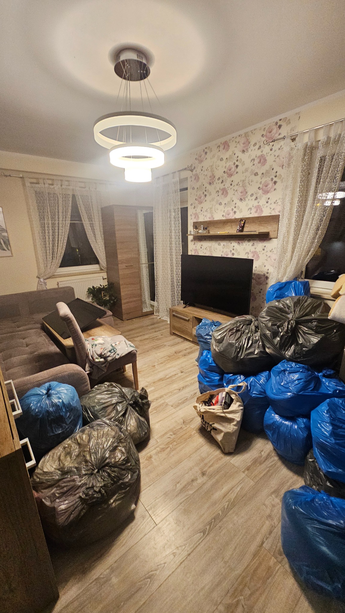 Pokój przed opróżnianiem: worki na podłodze, meble w tle. Widoczny etap przygotowań do transportu, z workami spakowanymi rzeczami, gotowymi do wyniesienia.