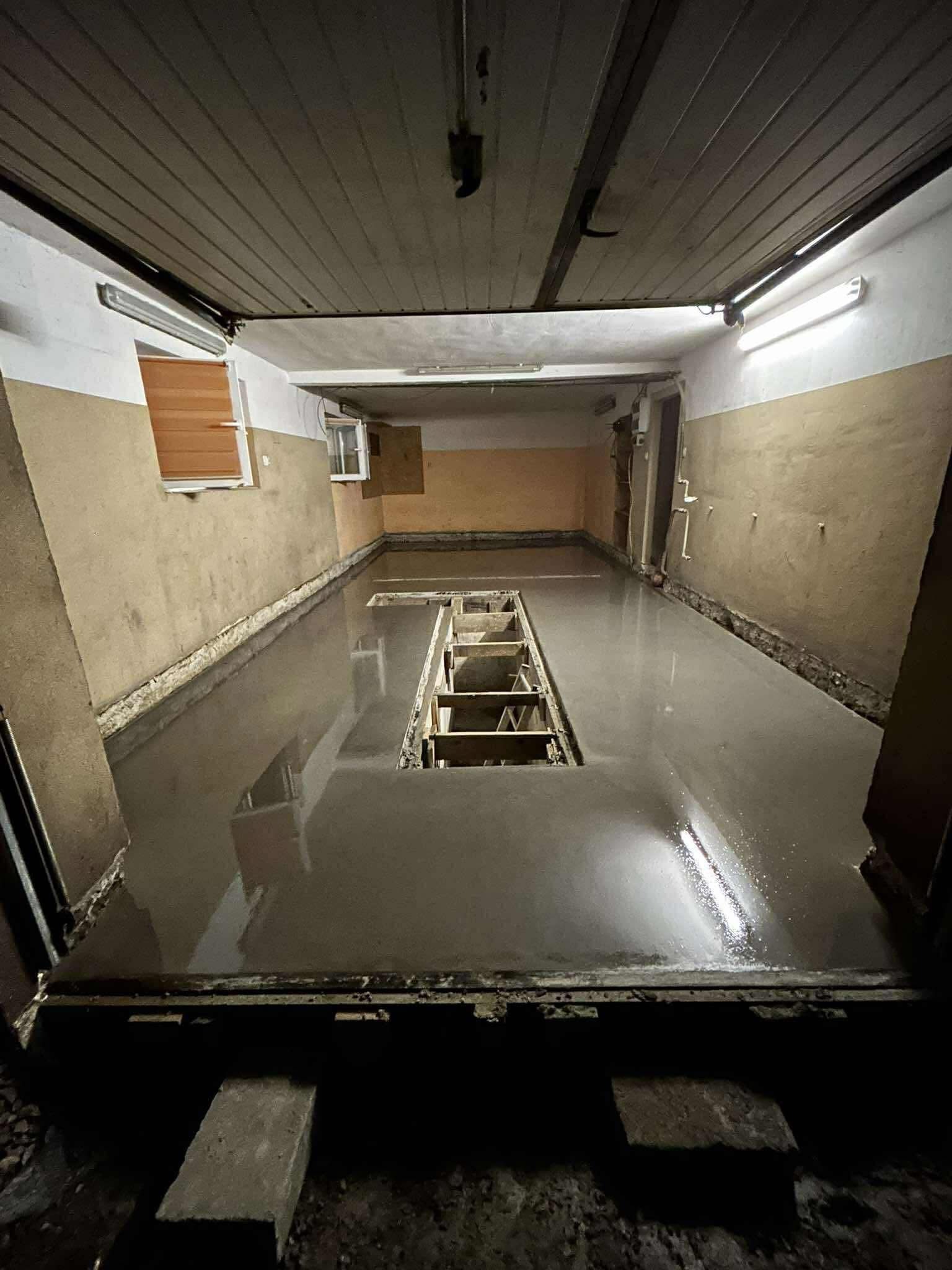 Świeżo wylana, gładka posadzka w pomieszczeniu z kanałem rewizyjnym. Widoczne oświetlenie jarzeniowe i fragmenty ścian w odcieniach beżu i bieli.