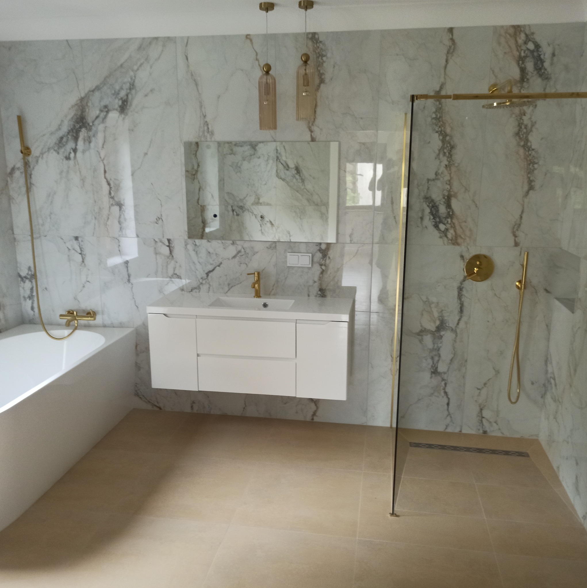 Elegancka łazienka z marmurowymi płytkami, złotą armaturą i białymi meblami. Kabina prysznicowa ze złotymi detalami. Nowoczesny design z dbałością o szczegóły.