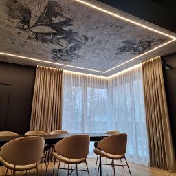 Deco Inspiration Joanna Michalak - Eleganckie, beżowe zasłony z delikatnej tkaniny, upięte przy oknie. Sufit z motywem roślinnym i oświetleniem LED. Wnętrze jadalni z krzesłami i stołem.