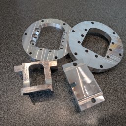 JTH - Precyzyjnie obrobione, srebrne elementy metalowe po obróbce CNC, leżące na szarej powierzchni. Widoczne ślady obróbki skrawaniem.