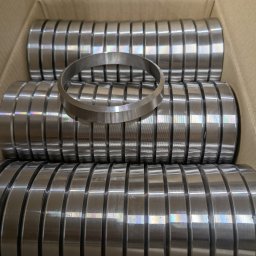 JTH - Metalowe pierścienie w kartonowym pudełku, jeden pierścień leży na wierzchu. Widoczne ślady po obróbce. Precyzyjne wykonanie detali.