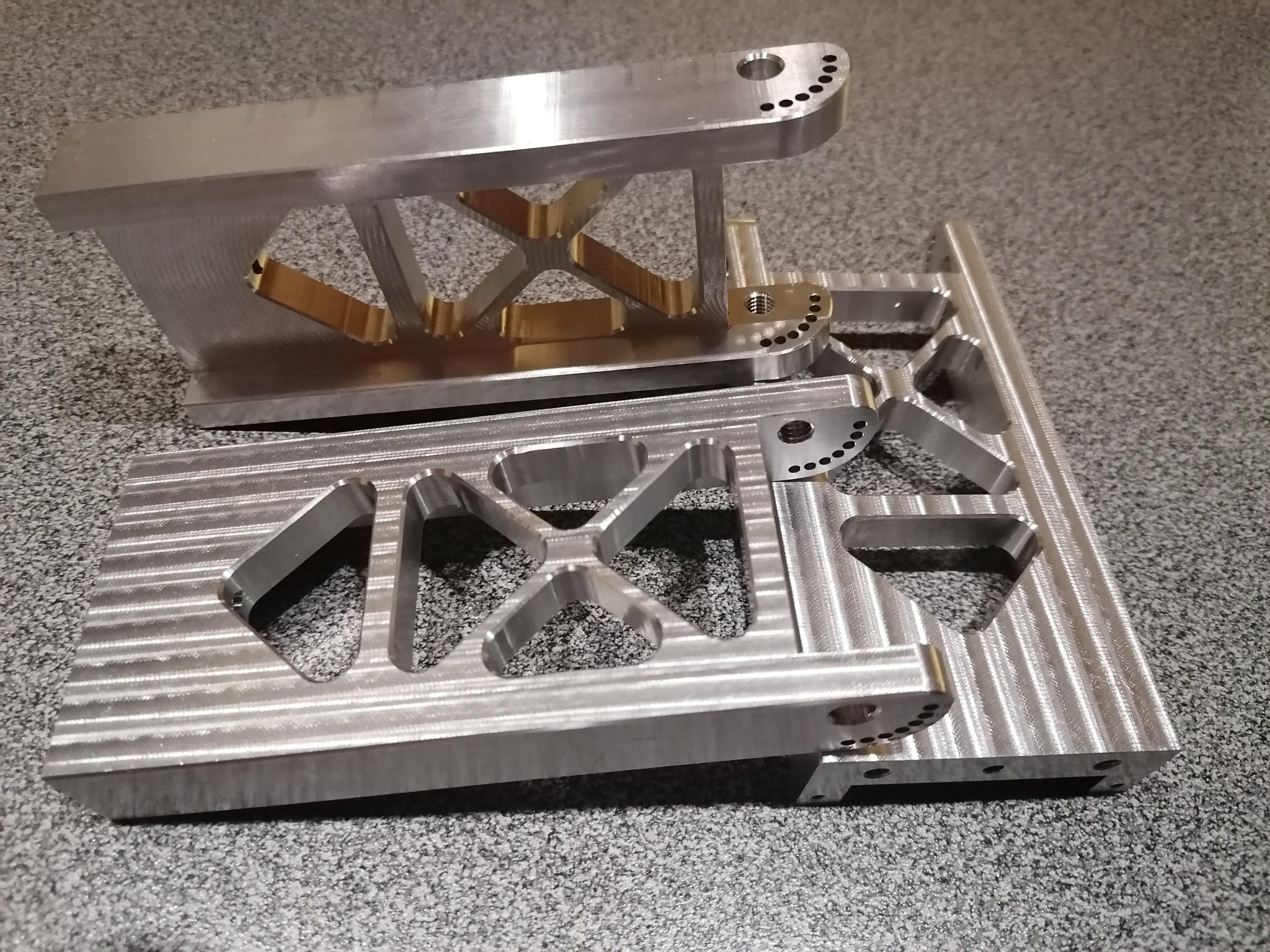 Precyzyjnie obrobione, srebrne elementy metalowe z licznymi otworami, ukazujące detale obróbki CNC na szarym tle. Widoczne ślady po frezowaniu.