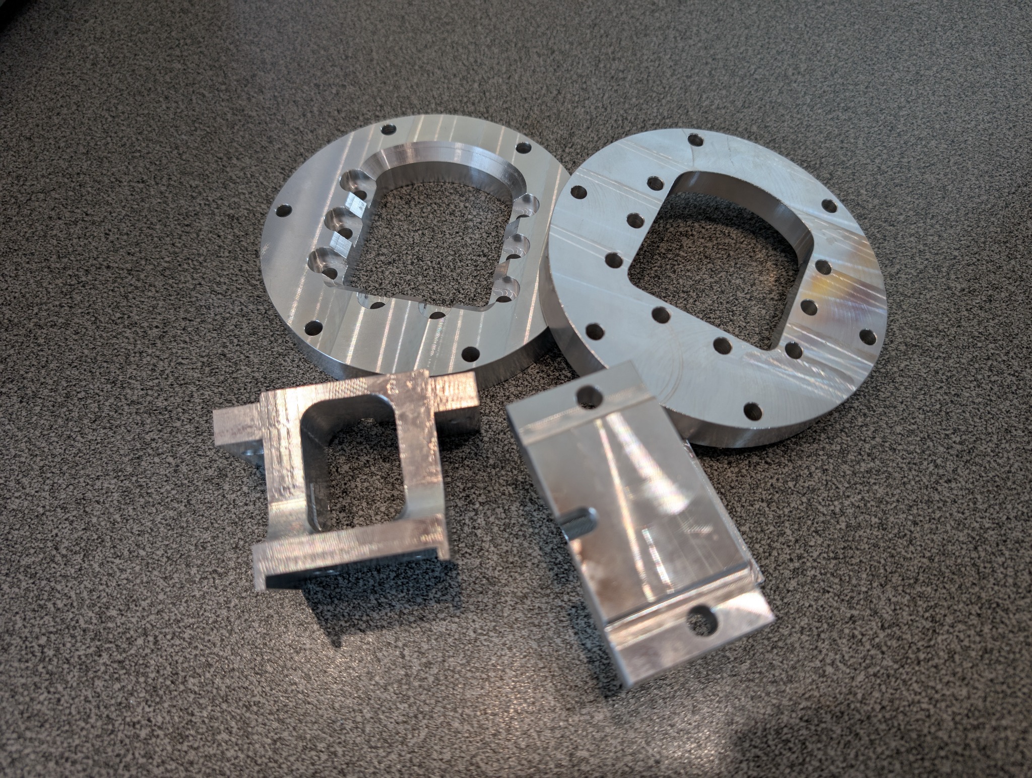 Precyzyjnie obrobione, srebrne elementy metalowe po obróbce CNC, leżące na szarej powierzchni. Widoczne ślady obróbki skrawaniem.