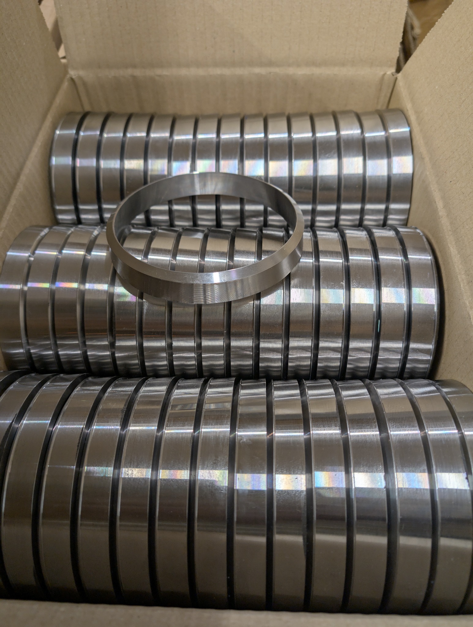 Metalowe pierścienie w kartonowym pudełku, jeden pierścień leży na wierzchu. Widoczne ślady po obróbce. Precyzyjne wykonanie detali.