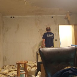 Daniel Starski Usługi Ogólnoremontowe i Ogrody - Przygotowanie ścian do malowania: usunięte stare tapety, widoczny pracownik w pomieszczeniu z drabiną i stołkiem. Ściany wymagają dalszej obróbki.