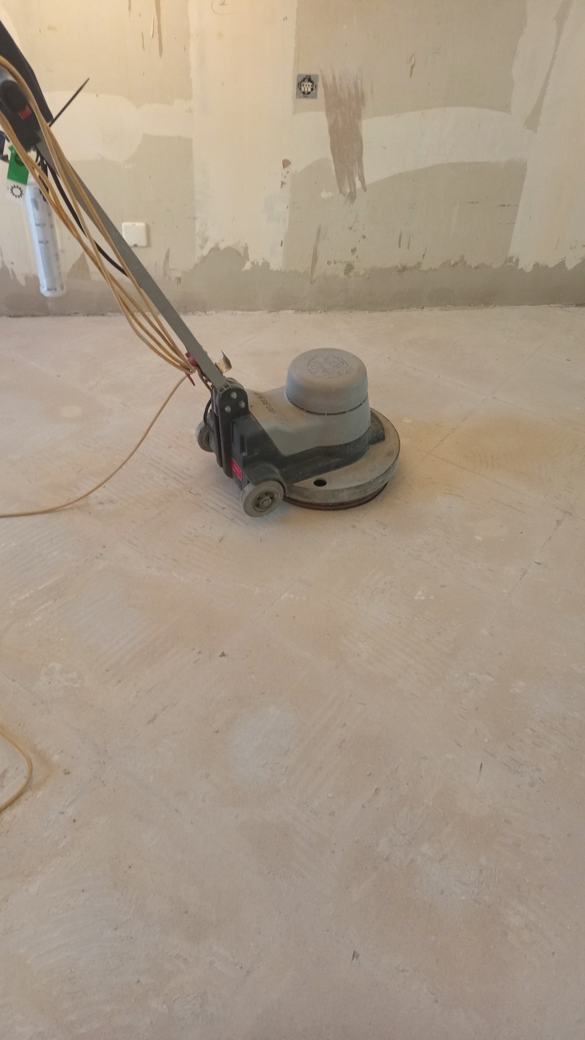 Szlifowanie podłogi maszyną w pomieszczeniu przed malowaniem ścian. Widoczne ślady po szlifowaniu i przygotowaniu podłoża. Przygotowanie do prac wykończeniowych.