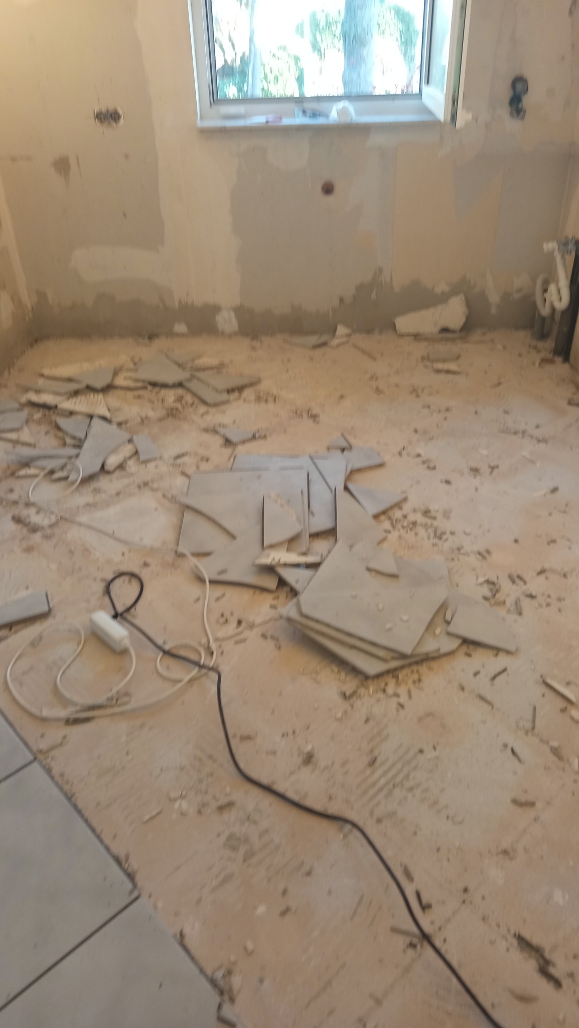 Remont pokoju: przygotowanie ścian do malowania, widoczne ślady po usuniętych płytkach, gruz na podłodze, okno w tle. Prace wykończeniowe w trakcie.