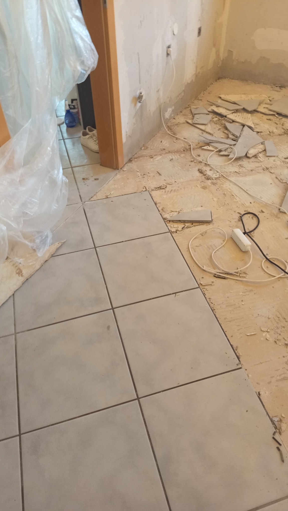 Układanie płytek podłogowych w Cieszynie. Częściowo ułożona podłoga z szarych płytek, widoczne pozostałości po starych płytkach i przygotowanie do dalszych prac.