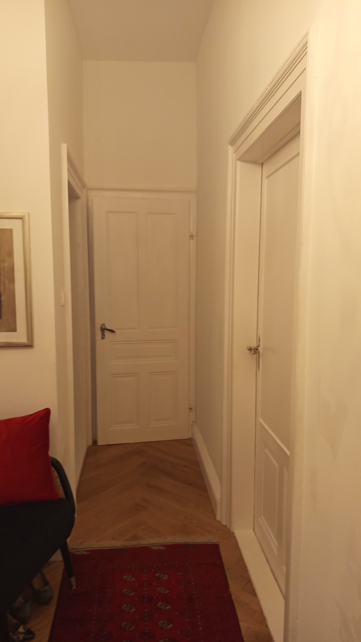 Biały korytarz po malowaniu z parkietem w jodełkę i czerwonym dywanem. Widoczne dwie białe, drewniane drzwi i fragment obrazu w złotej ramie.