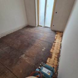 Tad-pol - Cyklinowanie podłogi w trakcie realizacji. Część podłogi wycyklinowana, widoczna maszyna do cyklinowania. Okno zabezpieczone folią malarską.