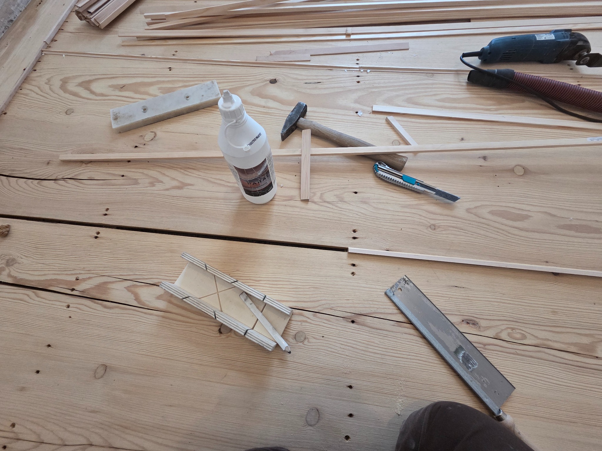Jasne drewno podłogowe w trakcie prac wykończeniowych z narzędziami: młotek, piła, klej, listwy przypodłogowe i elektryczne narzędzie wielofunkcyjne.