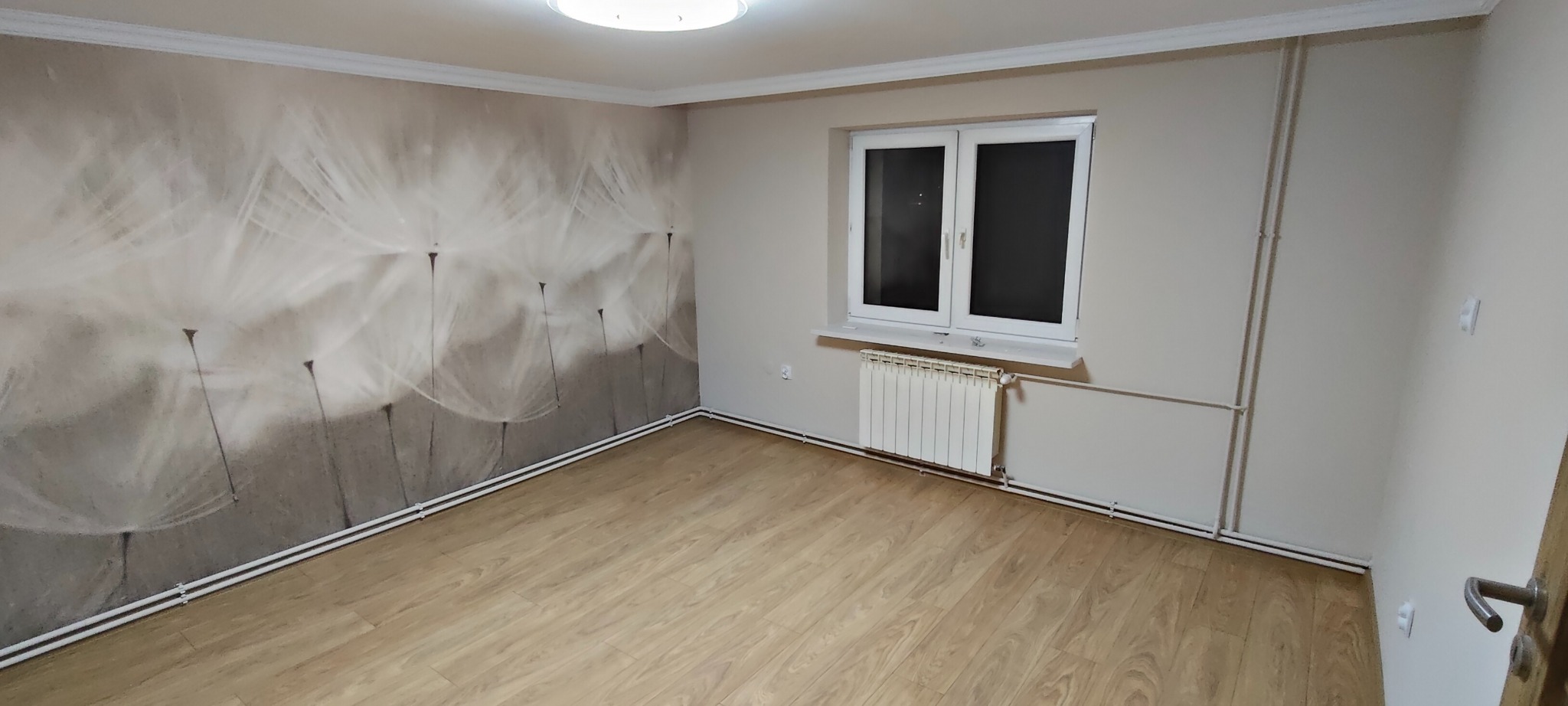 Pokój po remoncie: jasne panele, ściana z motywem dmuchawca, białe okno i grzejnik. Listwy przypodłogowe i sufitowe. Nowoczesne wykończenie wnętrza.