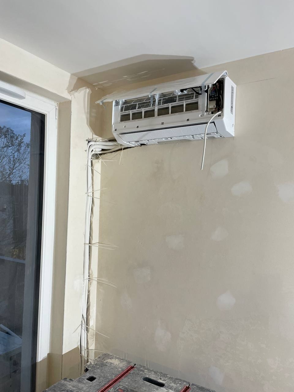 Montaż klimatyzacji w domu: biały klimatyzator na ścianie, widoczne przewody zabezpieczone opaskami, przygotowana ściana do malowania, drabina robocza.