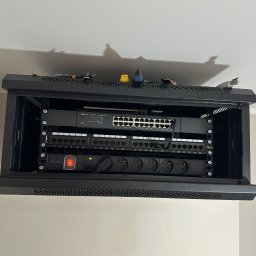 NETHOME MARCIN KOSTRZEWSKI - Zamknięta szafa rack 19 cali z zainstalowanym switchem TP-Link, panelem krosowniczym i listwą zasilającą Lanberg. Widoczne kable i złącza. Górna część szafy z narzędziami.