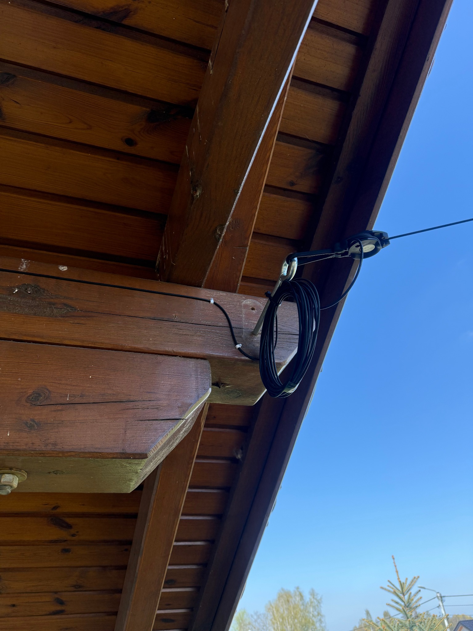 Napowietrzne przyłącze światłowodowe zamontowane do drewnianej konstrukcji dachu, widoczne mocowania i zwój kabla na tle błękitnego nieba.
