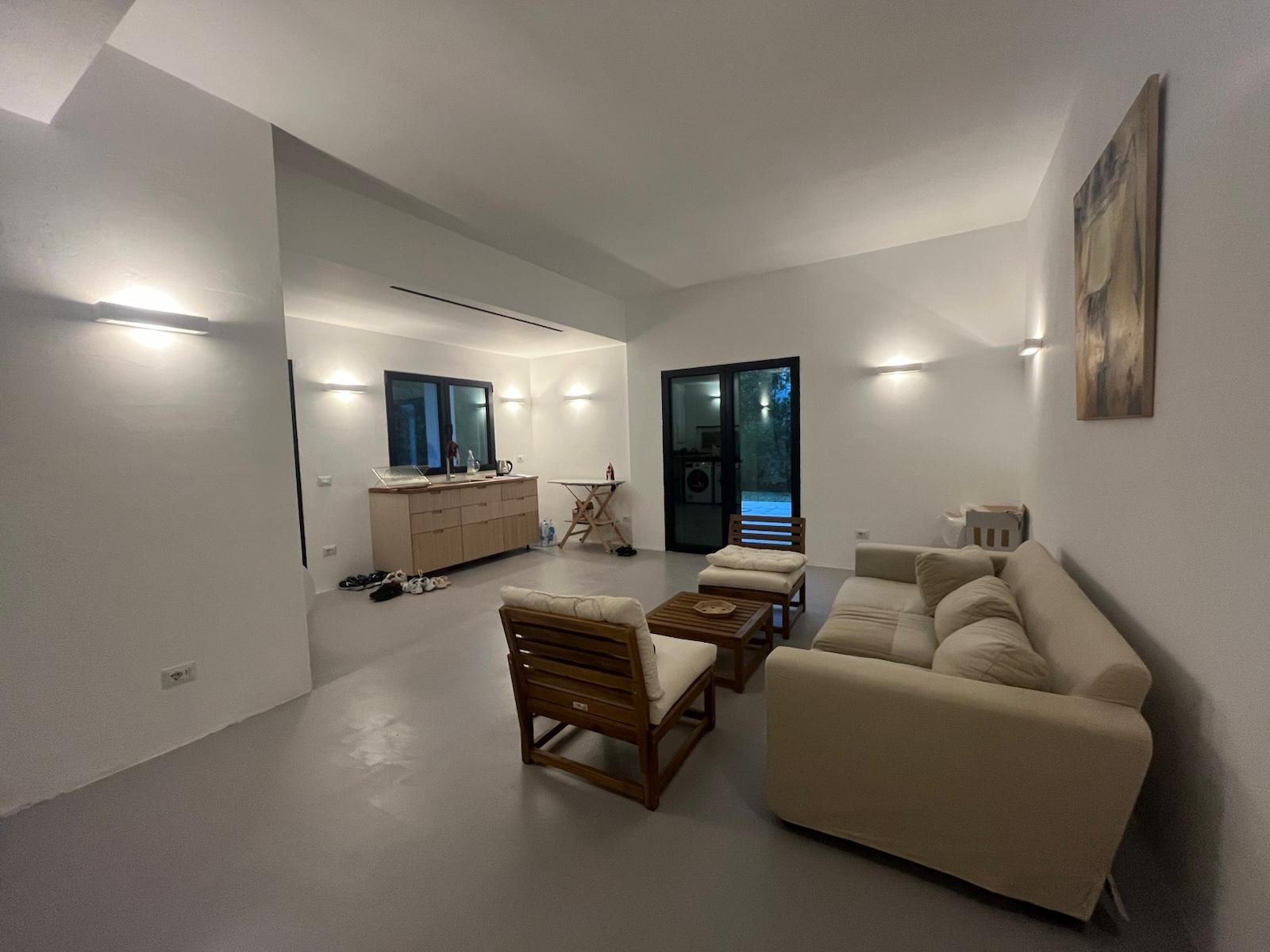 Jasne, minimalistyczne wnętrze z szarą podłogą, drewnianymi meblami i białymi ścianami. Widoczne oświetlenie punktowe i obraz na ścianie. Nowoczesny design.