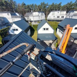 Klimler Leraczyk Marcin - Widok z podnośnika koszowego na osiedle domów jednorodzinnych z ciemnymi dachami w słoneczny dzień. W kadrze fragment urządzenia podnośnika.