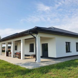 Mateusz Laskowski - Biały budynek z kolumnami i ciemną dachówką, widok z zewnątrz, błękitne niebo w tle. Na podłożu widoczne płyty chodnikowe i trawa.