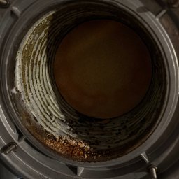 Term-Gaz - Wnętrze kotła gazowego z widocznymi śladami korozji i osadów. Spiralne żebrowanie i metalowa obudowa. Widoczne ślady zużycia i zabrudzenia.