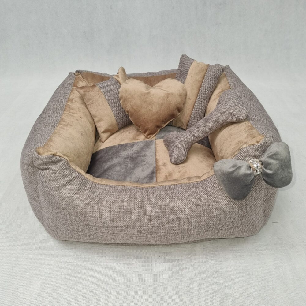 Beżowo-szare legowisko dla psa z poduszkami w kształcie serca i kości, ozdobione kokardą z cyrkoniami, na jasnym tle. Widok z przodu, miękkie światło.