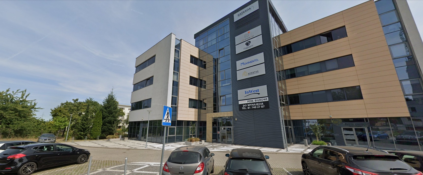 Nowoczesny budynek biurowy z logo firm: Kaskada, InWest, Movimento. Tablica informacyjna o wynajmie powierzchni biurowej. Widok z parkingu.
