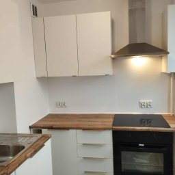 VENLOP SPÓŁKA Z OGRANICZONĄ ODPOWIEDZIALNOŚCIĄ - Nowoczesna kuchnia z białymi szafkami i drewnianym blatem. Czarna płyta indukcyjna i piekarnik w zabudowie. Minimalistyczny design z oświetleniem punktowym.