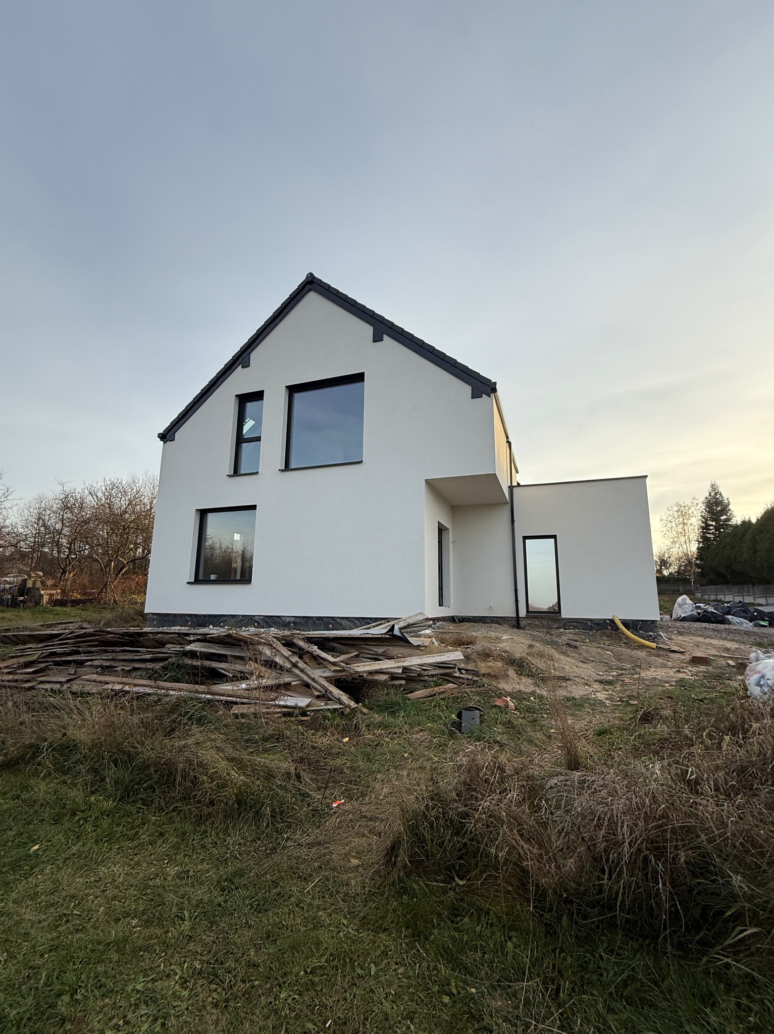 Biały dom z czarnymi ramami okiennymi w Ogrodzieńcu, po świeżo wykonanych pracach elewacyjnych. Widoczne deski i trawa na pierwszym planie, błękitne niebo w tle.