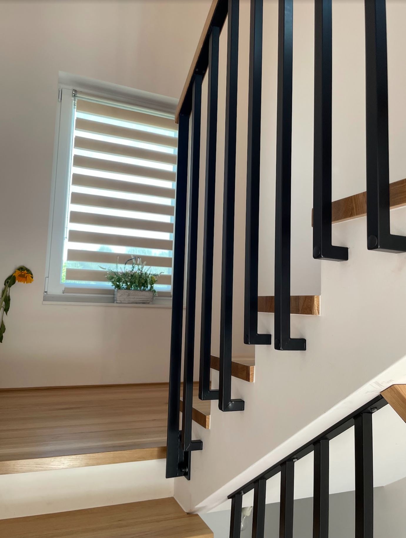 Nowoczesna balustrada schodowa z czarnymi, metalowymi słupkami i drewnianym poręczą, w jasnym wnętrzu domu jednorodzinnego. Widok z dołu na schody.
