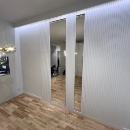 Just Perfect - Nowoczesna szafa wnękowa z lustrzanymi drzwiami przesuwnymi i dekoracyjnymi panelami ściennymi. Parkiet na podłodze, oświetlenie LED na suficie.