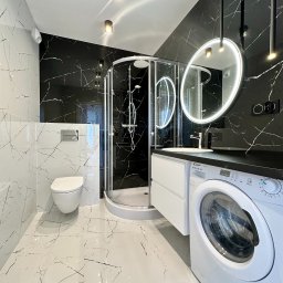 Just Perfect - Nowoczesna łazienka w czarno-białej kolorystyce z kabiną prysznicową, toaletą, umywalką z podświetlanym lustrem i pralką. Marmurowe płytki na ścianach i podłodze.