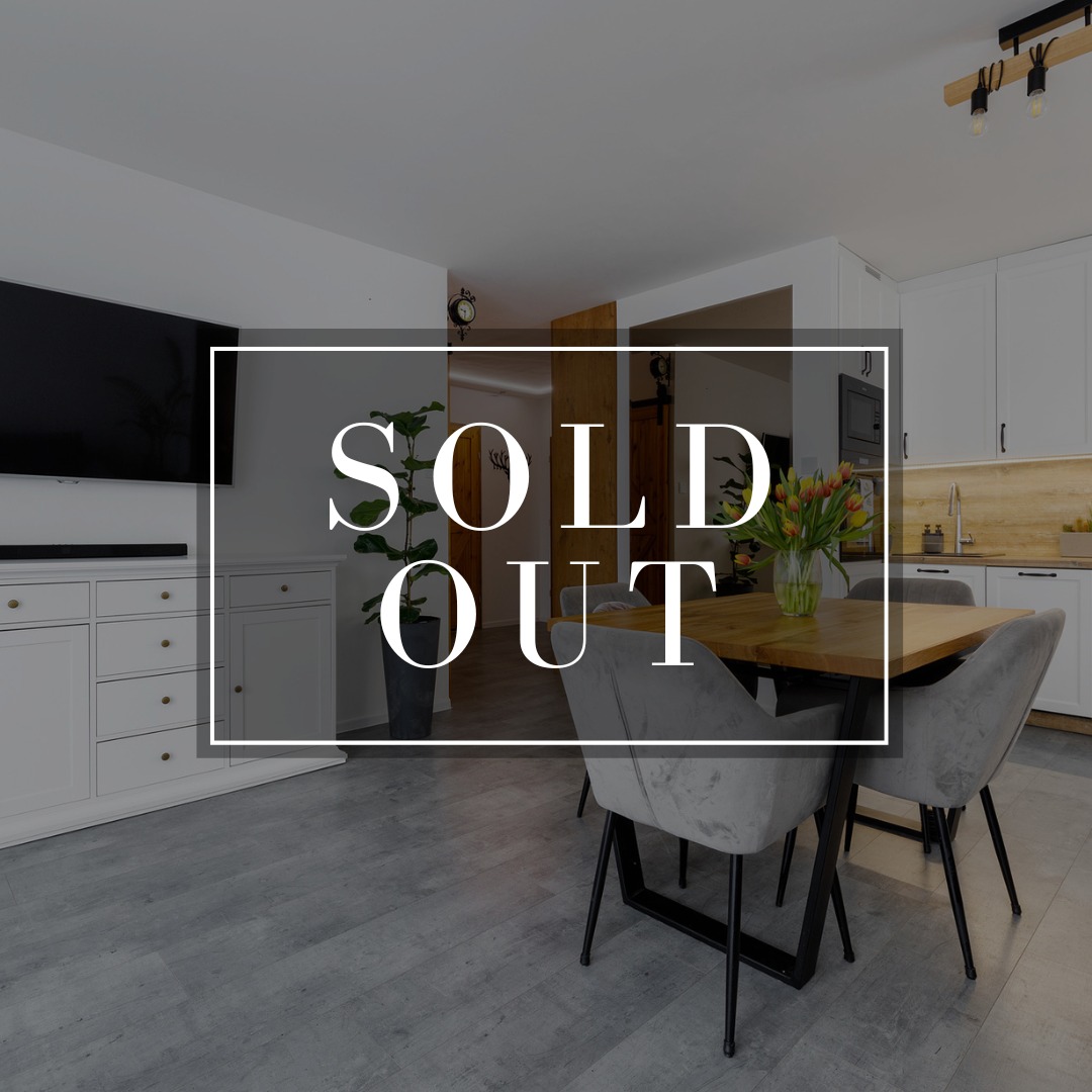 Jasne wnętrze z napisem 'SOLD OUT': salon z telewizorem, jadalnia z kwiatami i kuchnia w tle. Nowoczesny design, szare podłogi, ciepłe oświetlenie.