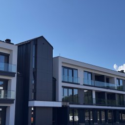 ŚWIAT SZKŁA SPÓŁKA Z OGRANICZONĄ ODPOWIEDZIALNOŚCIĄ - Nowoczesny budynek wielorodzinny z balkonami zabezpieczonymi szkłem, w odcieniach bieli i szarości, na tle błękitnego nieba. Widok z dołu, podkreślający architekturę.