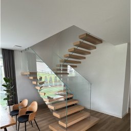 ŚWIAT SZKŁA SPÓŁKA Z OGRANICZONĄ ODPOWIEDZIALNOŚCIĄ - Nowoczesne schody drewniane z przezroczystą taflą szkła jako balustradą, w jasnym wnętrzu domu. Widok z dołu, podkreślający minimalistyczny design i naturalne światło.