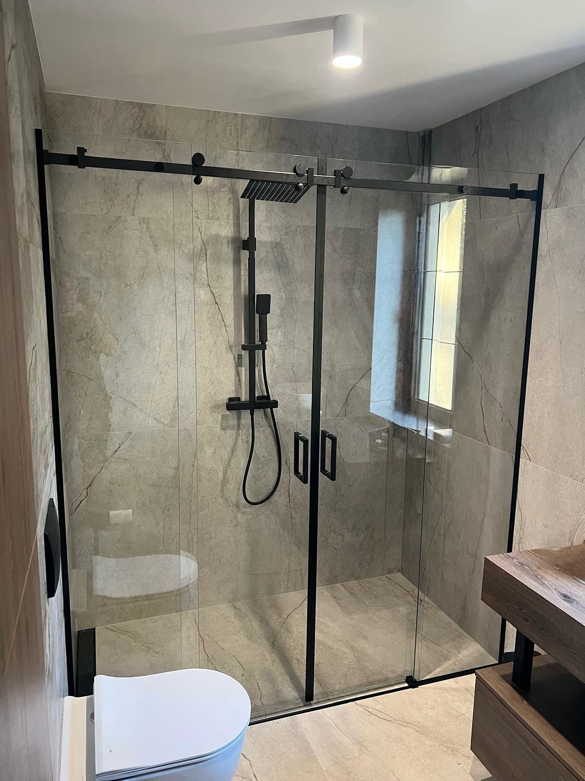 Nowoczesna kabina prysznicowa z przesuwnymi drzwiami, czarne profile, szklane ściany, Bielsko-Biała. Minimalistyczny design, widoczna armatura i fragment toalety.