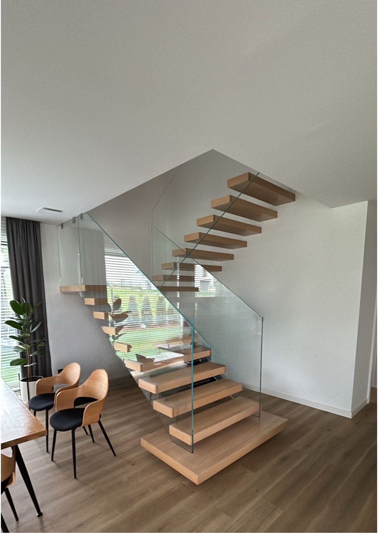 Nowoczesne schody drewniane z przezroczystą taflą szkła jako balustradą, w jasnym wnętrzu domu. Widok z dołu, podkreślający minimalistyczny design i naturalne światło.