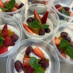 OKR DIET - Deser chia w przezroczystych pojemnikach z truskawkami, winogronami, mango i miętą. Gotowe porcje cateringu dietetycznego, widok z góry, jasne oświetlenie.