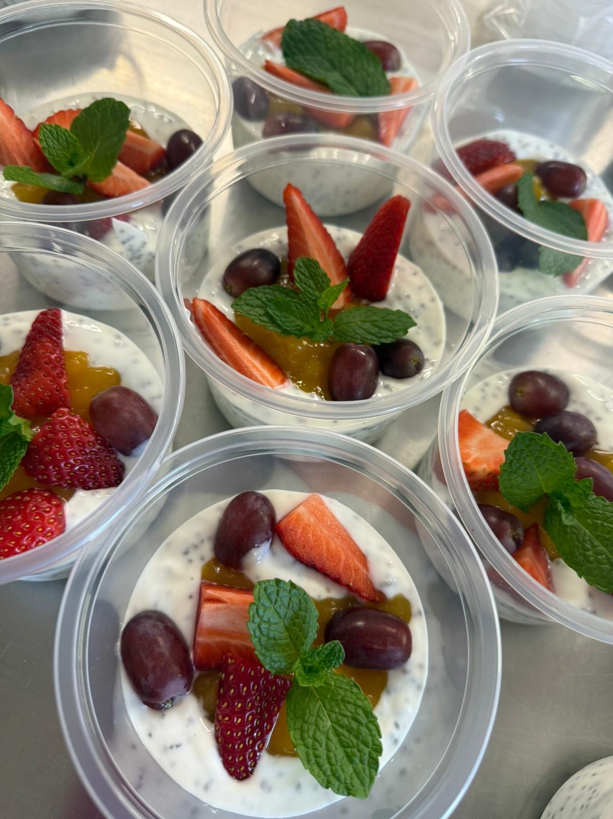 Deser chia w przezroczystych pojemnikach z truskawkami, winogronami, mango i miętą. Gotowe porcje cateringu dietetycznego, widok z góry, jasne oświetlenie.