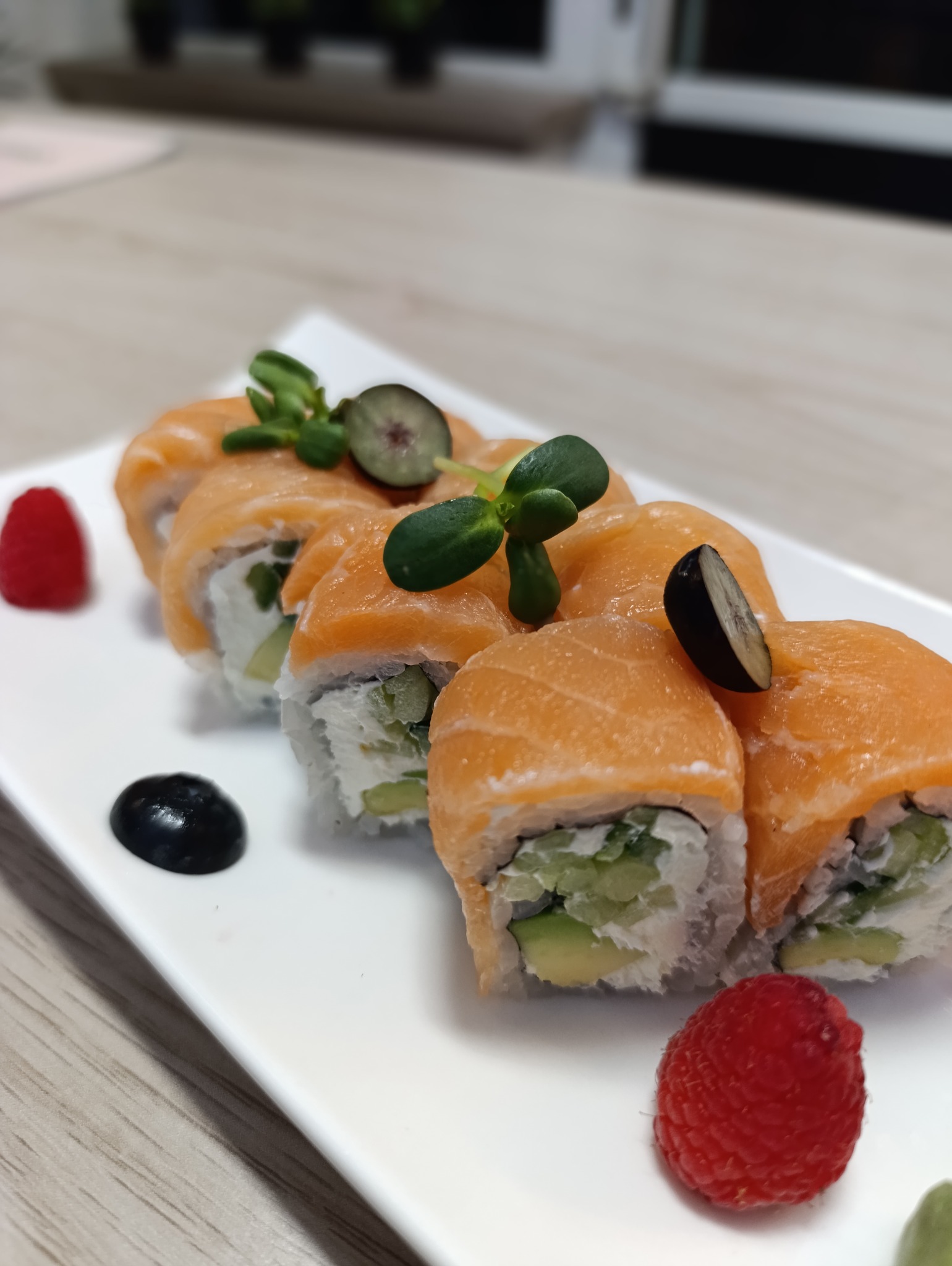 Elegancko podane sushi z łososiem, awokado i kremowym serem, udekorowane świeżymi ziołami i owocami na białym talerzu. Bliski kadr, ostre detale.