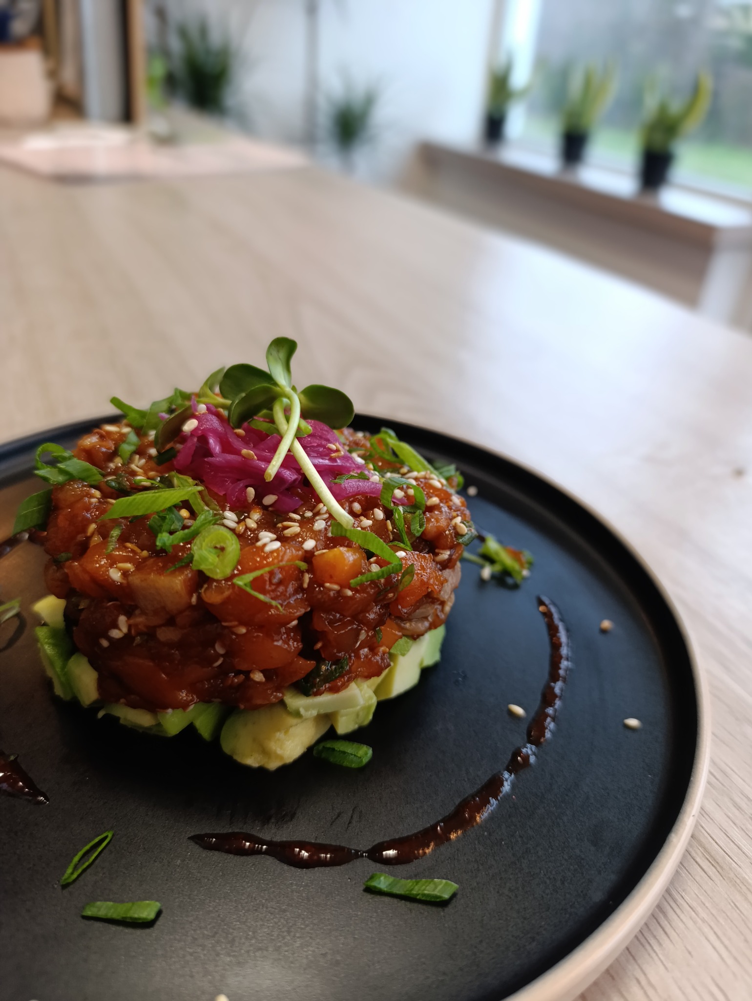 Tartar z tuńczyka na awokado, udekorowany kiełkami i sosem balsamicznym na czarnym talerzu. Elegancka prezentacja dania cateringowego.