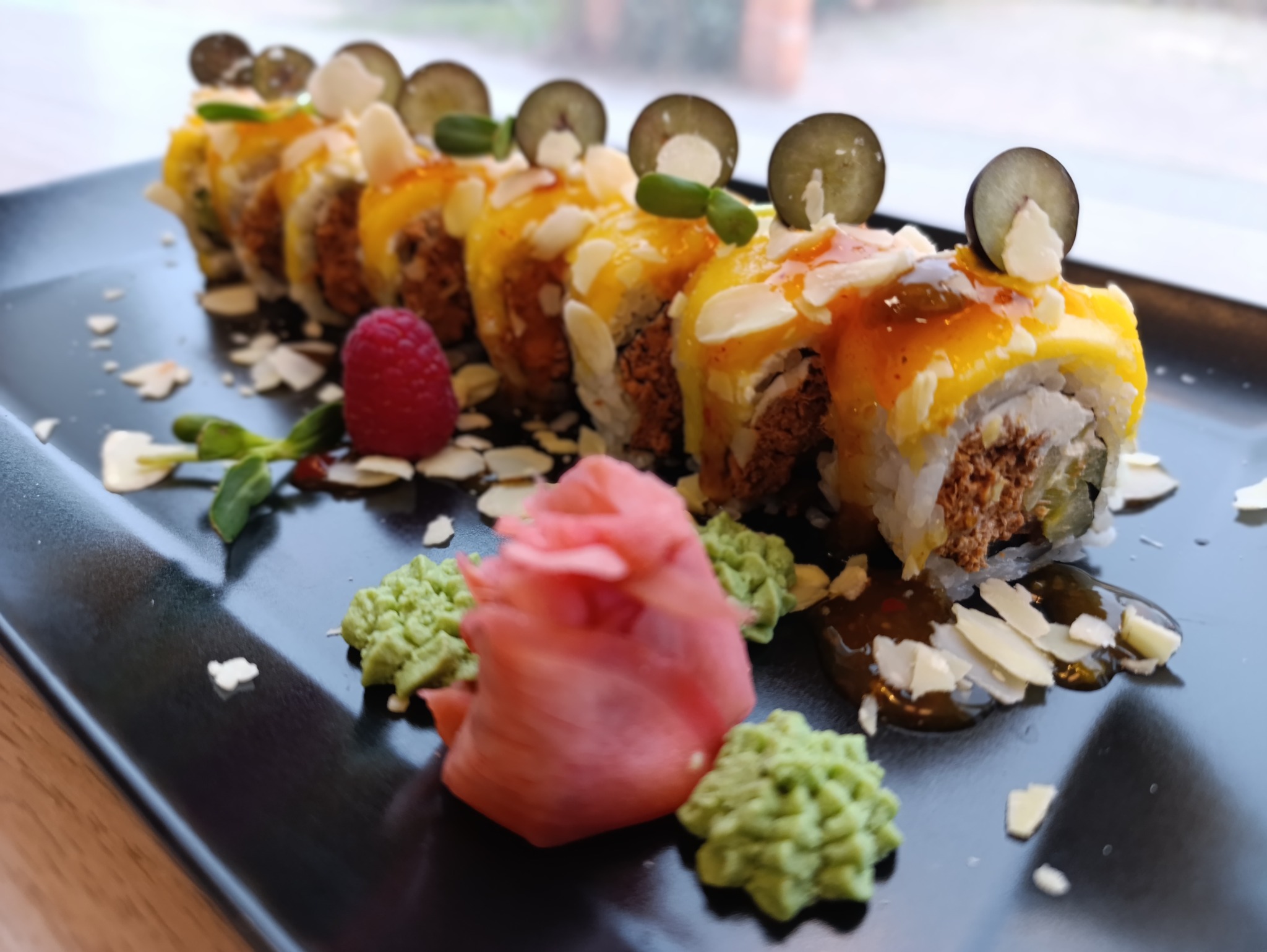 Egzotyczne sushi z mango, migdałami i borówkami na czarnym talerzu, udekorowane imbirem i wasabi. Elegancka kompozycja kulinarna.