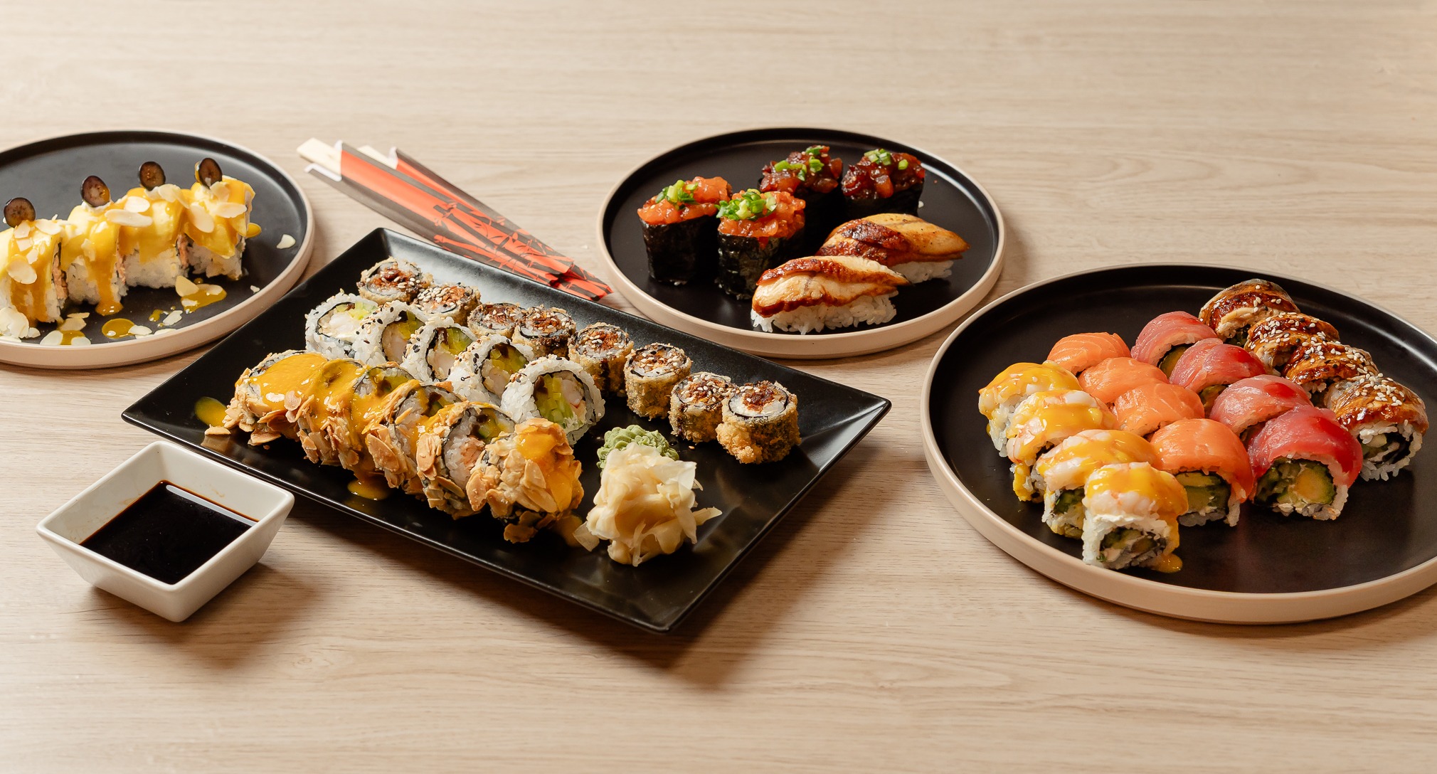 Zestaw sushi: rolki z łososiem, tuńczykiem, węgorzem, krewetką i warzywami, podane na czarnych talerzach z sosem sojowym i imbirem na drewnianym stole.