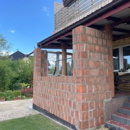 Renowo Dawid Sala - Murowana ściana z czerwonej cegły na zewnątrz budynku w trakcie budowy, widoczne okno i fragment dachu. Prace murarskie w toku, świeża zaprawa.