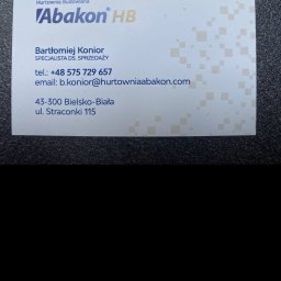 MONTAŻ PROJEKT Bartłomiej Konior - Wizytówka Hurtowni Budowlanej Abakon HB z Bielska-Białej. Dane kontaktowe: Bartłomiej Konior, telefon, email, adres. Tło wizytówki zdobione subtelnym wzorem.