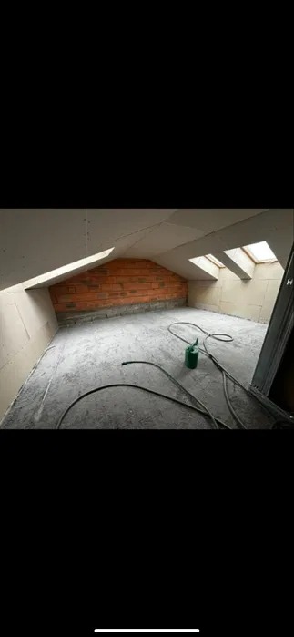 Poddasze w trakcie adaptacji: ściany z płyt gipsowych, fragment muru z cegły, betonowa podłoga, okna dachowe i zielony kanister. Widok na surowy stan wnętrza.