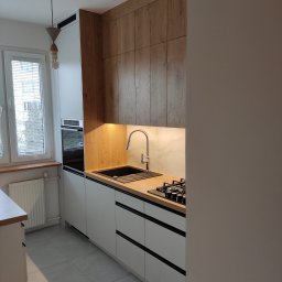 DECHA - Nowoczesna kuchnia z drewnianymi szafkami górnymi i białymi dolnymi, czarnymi akcentami. Uwagę przykuwa oświetlenie LED pod szafkami i minimalistyczny design.