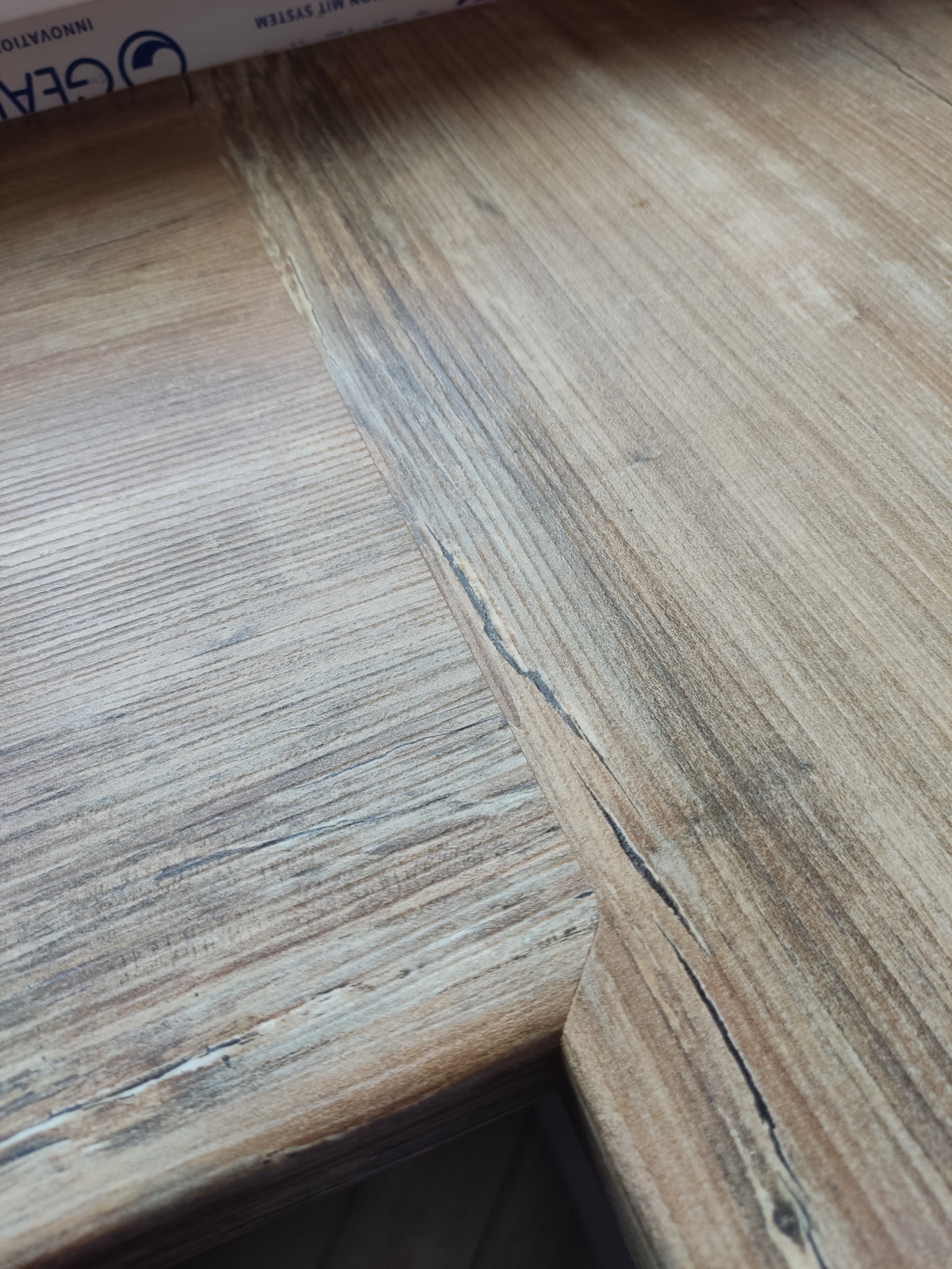 Zbliżenie na połączone panele podłogowe w odcieniach brązu i szarości, imitujące naturalne drewno z widocznymi słojami i delikatną strukturą.