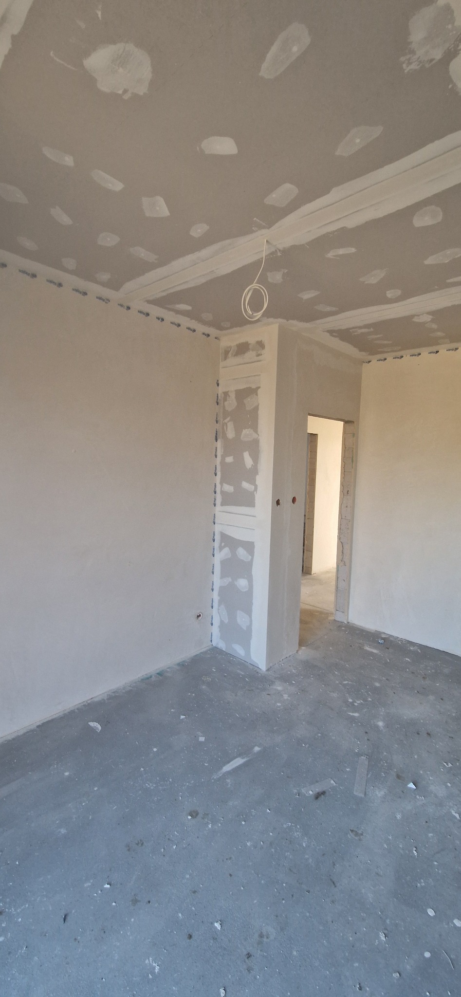 Surowe wnętrze w trakcie prac wykończeniowych: ściany i sufit pokryte gładzią, widoczne łączenia płyt karton-gips, przygotowane do dalszych prac malarskich.